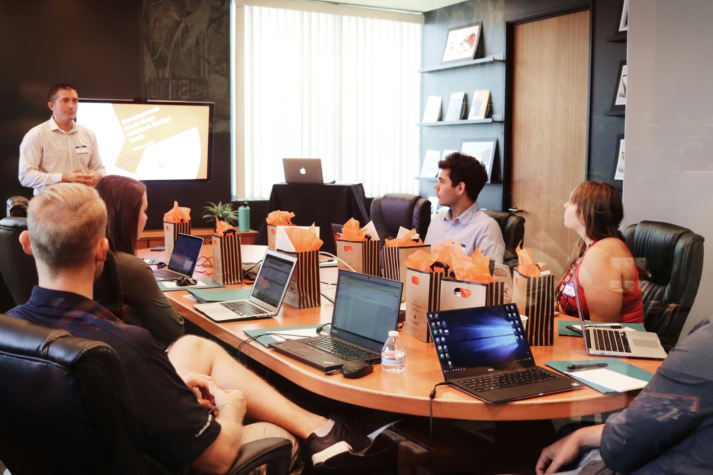 A presenter leading a hands-on workshop for a small group with laptops around a table